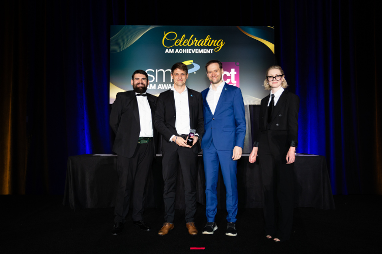 Preisverleihung TCT Hardware Award: Vier Personen auf der Bühne mit Trophäe vor dem Schriftzug „Celebrating AM Achievement"